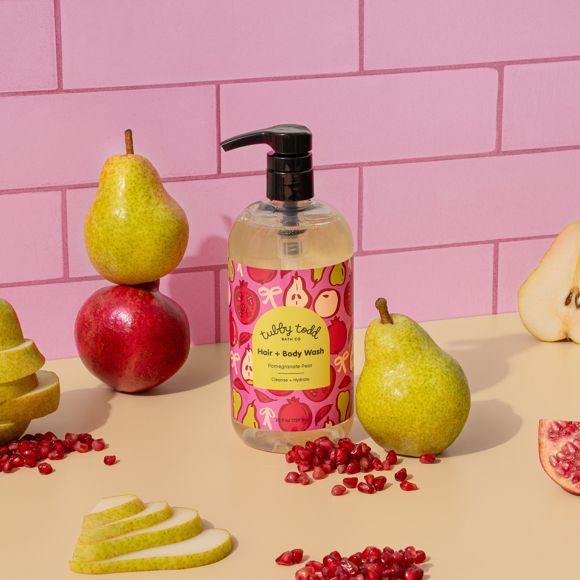 Pom Pear Hair + Body Wash 25oz bottle standing on pink and yellow color block background with surrounded pears and Pomegranates.